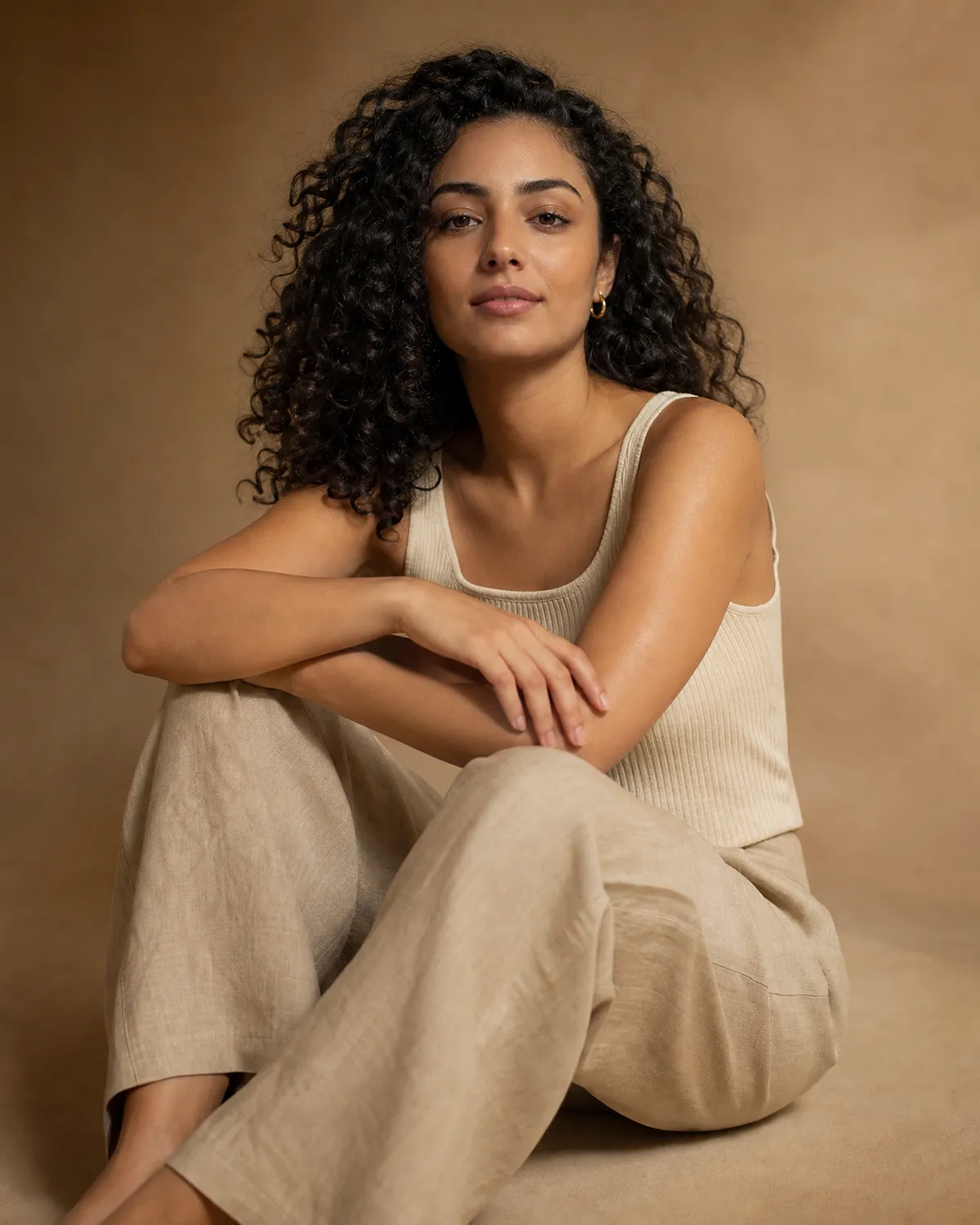 Femme aux cheveux bouclés assise, en camisole, bras et épaules dégagés