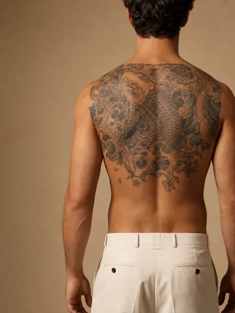Man seen from behind, a large black and grey tattoo across the upper half of his back, before laser tattoo removal in Sainte-Rose, Laval