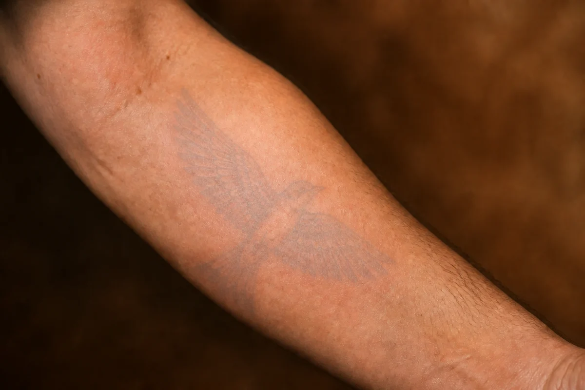 The same tattoo reduced to a bluish shadow on the forearm, still visible up close
