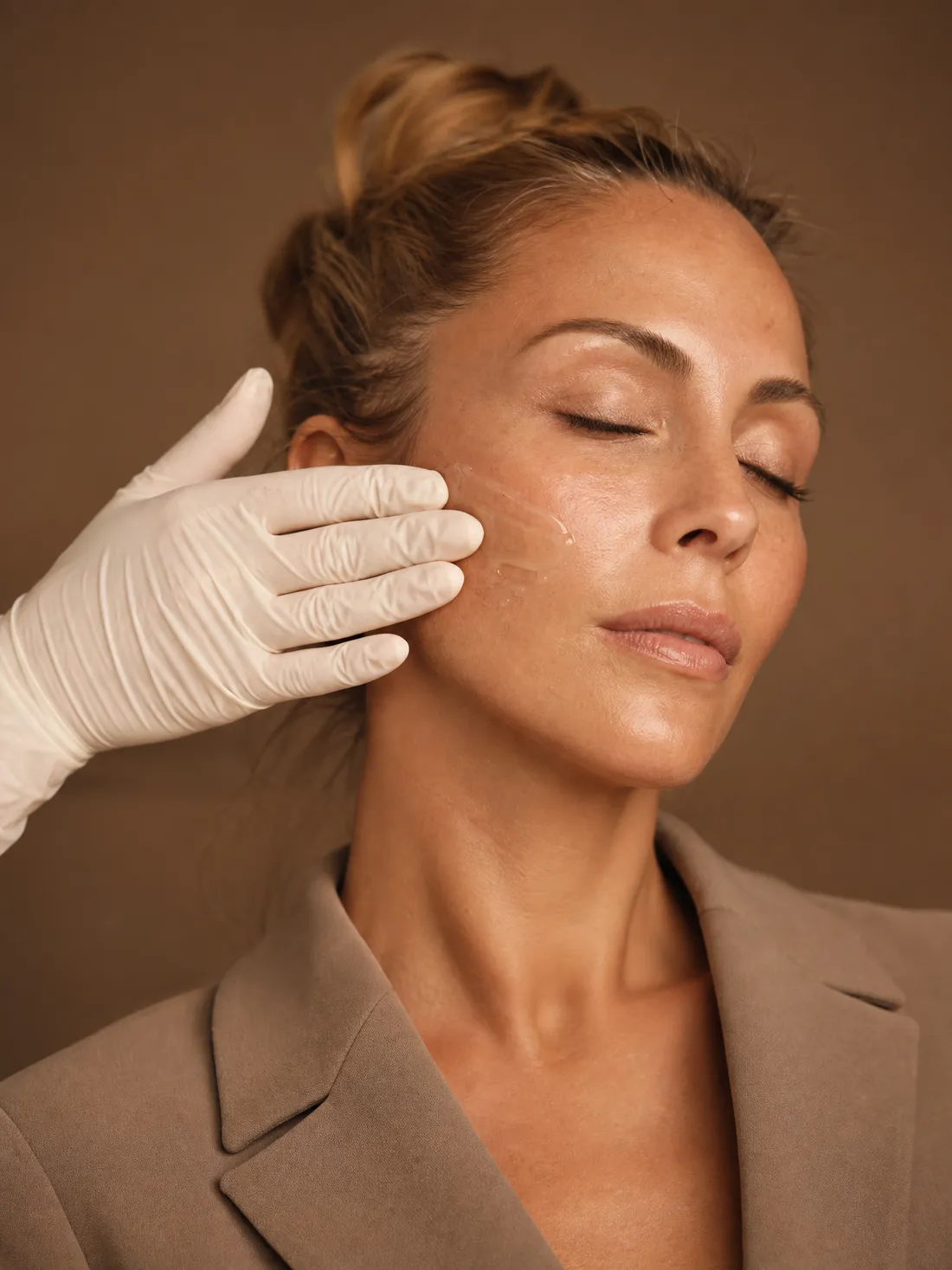 A gloved hand rests its palm on a woman's cheek, after a soothing product is applied